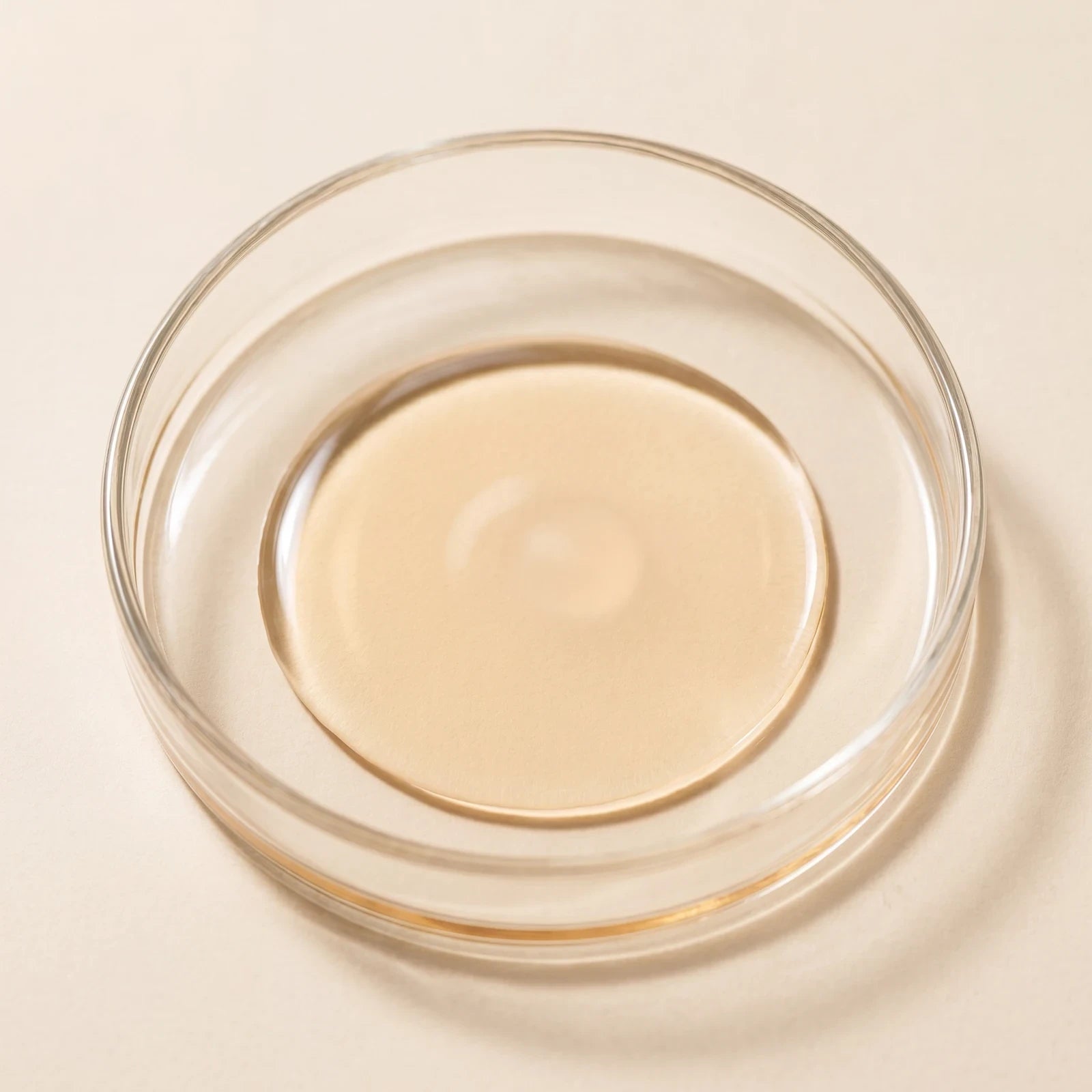 Pale-gold oil-soluble vitamin C ester in a glass dish on a cream ground.