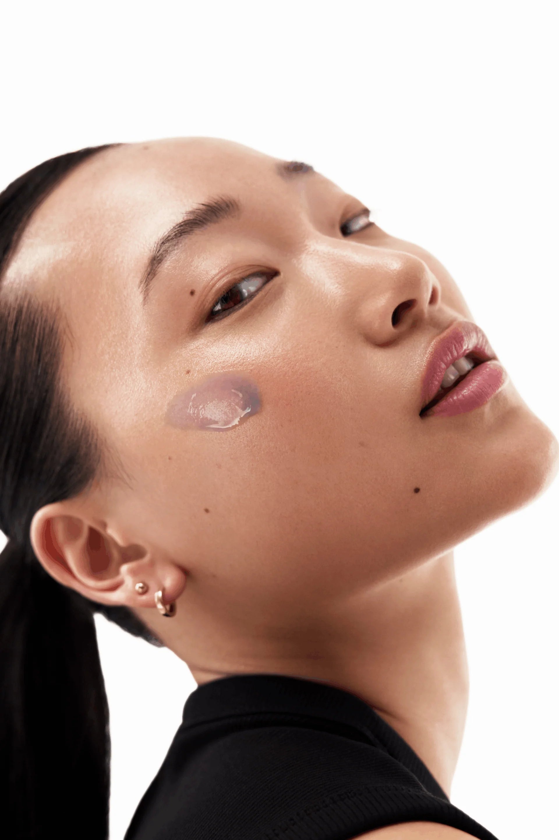 Neogen model with a bead of the botanical oil-serum resting on her cheek in warm directional light.