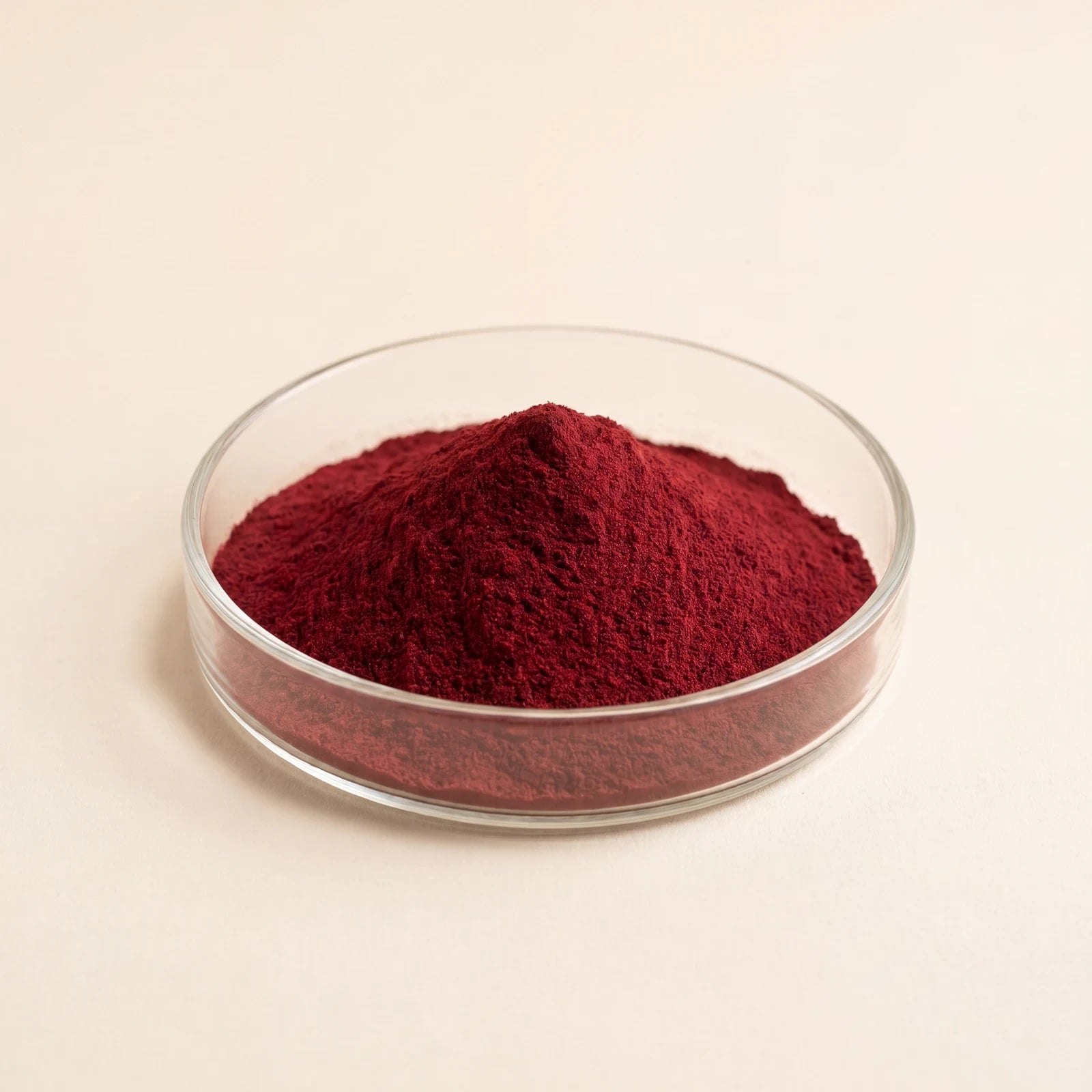 Deep-red astaxanthin powder in a glass dish on a cream ground.